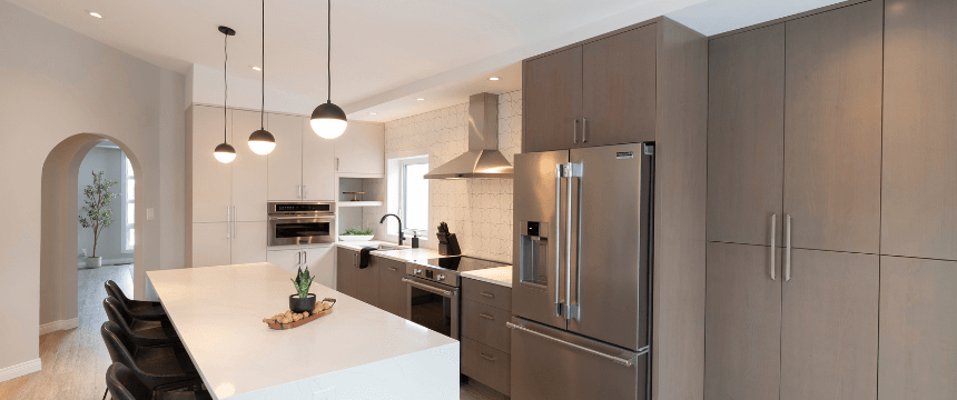 Renovating your forever home: A sleek, modern kitchen renovation featuring flat-panel, light brown cabinetry, a large white island, stainless steel appliances, and a textured tile backsplash.