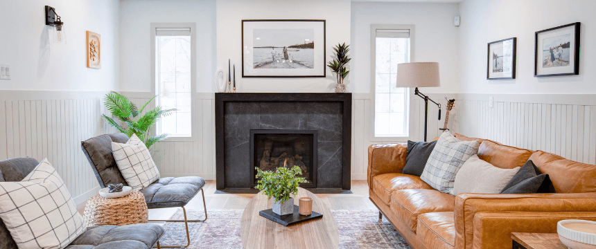 Renovating your forever home: A renovated living room with white vertical shiplap paneling, a dark marble-look fireplace surround, a brown leather sofa, and two gray accent chairs.