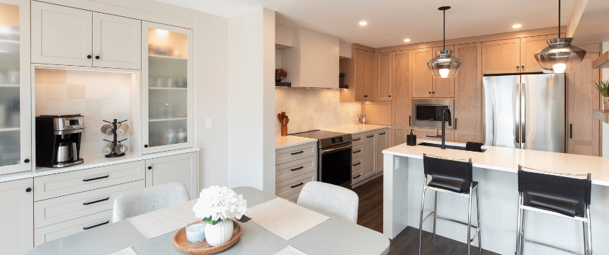 A kitchen renovation showing a light dining area with a view of the kitchen's two-toned wood and off-white cabinets and stainless steel refrigerator.