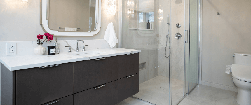 A luxurious primary bathroom renovation with a dark brown double vanity, a white marble-look countertop, and a glass-enclosed shower with chrome fixtures.