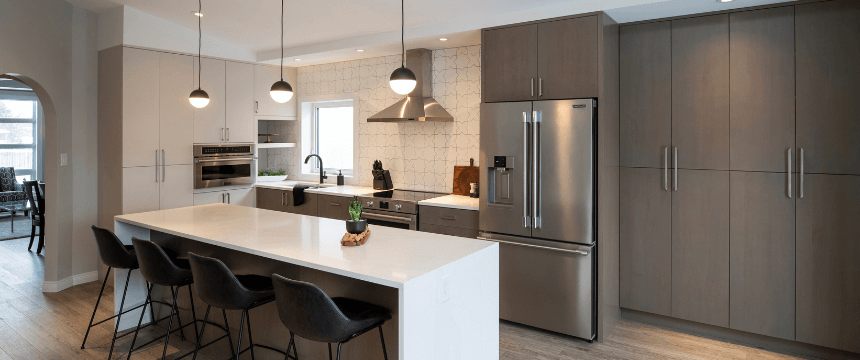 A sleek, modern kitchen renovation with tall, light brown flat-panel cabinets, a large white island with seating, and a patterned backsplash behind the range.